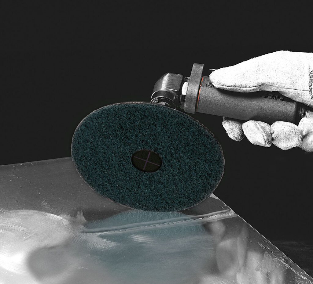 Self-adhesive sanding disc PSH on angle grinder while polishing a metal surface.