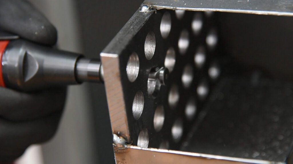 With a reverse deburr, a hole in a perforated metal profile is deburred by hand.