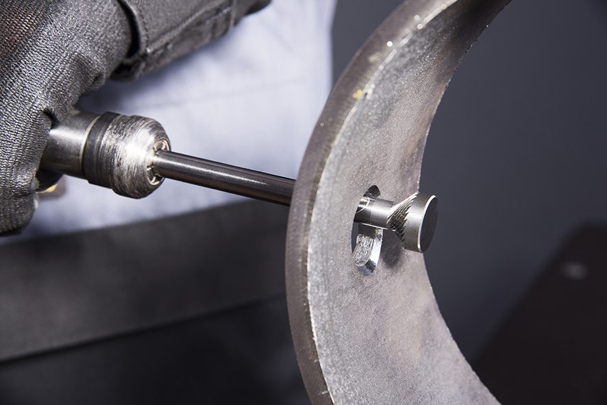 A reverse deburrer removes burrs from the back of a hole in a metal workpiece.